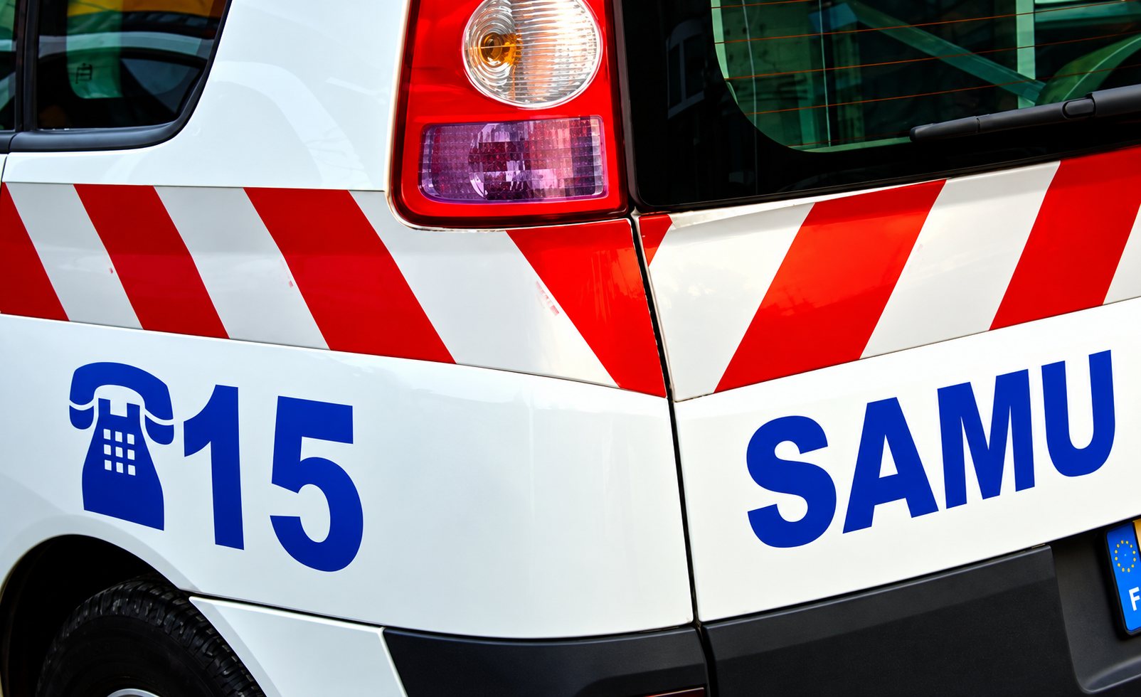 Arrière d’une ambulance du SAMU avec le numéro 15 et des bandes rouges et blanches.